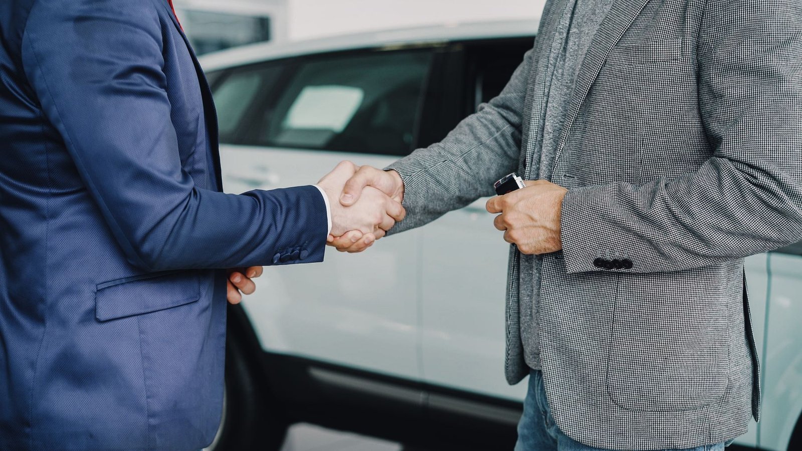 Two businessmen shaking hands in a car dealership, sealing a used car sale under the UAE VAT Profit Margin Scheme