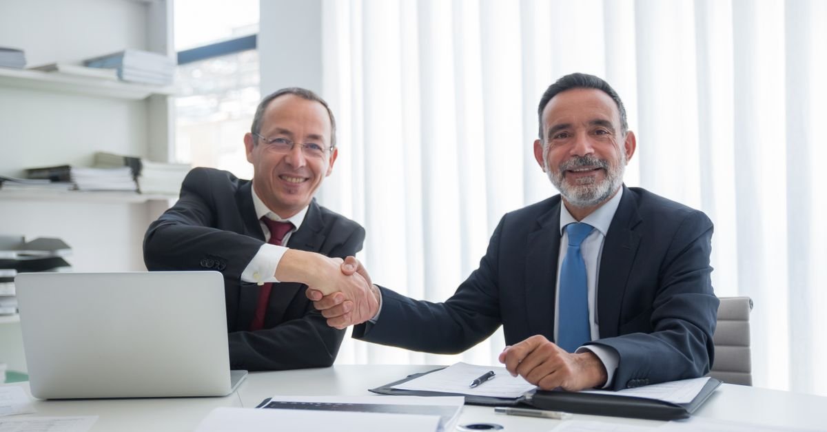 Two businessmen shaking hands over a signed agreement, representing a local service agent or corporate sponsor contract for a UAE mainland LLC