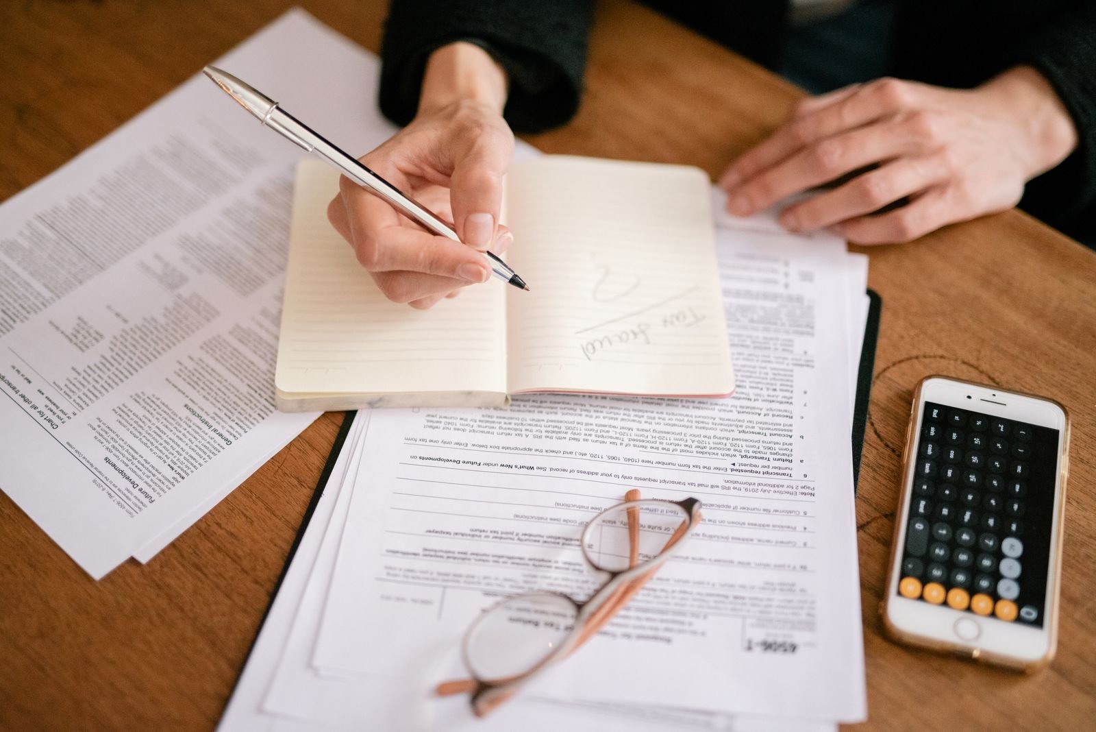 Close-up of a person writing in a notebook with tax documents and a calculator, representing UAE Corporate Tax Qualifying Group Relief documentation and record-keeping.