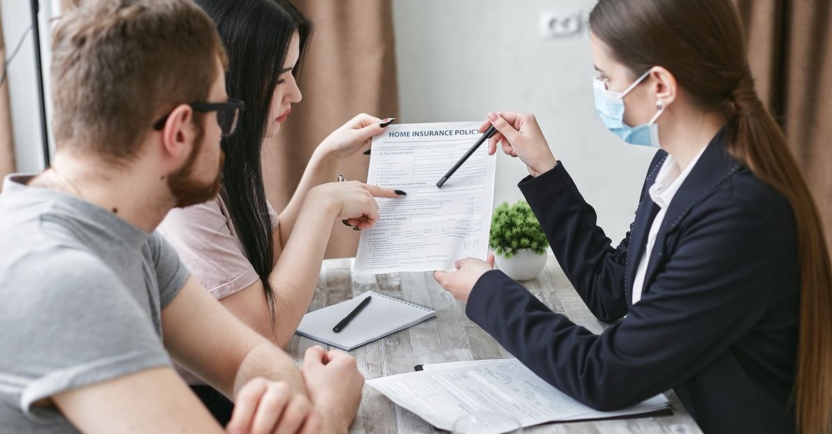 Three adults discuss a home insurance policy at a meeting table indoors