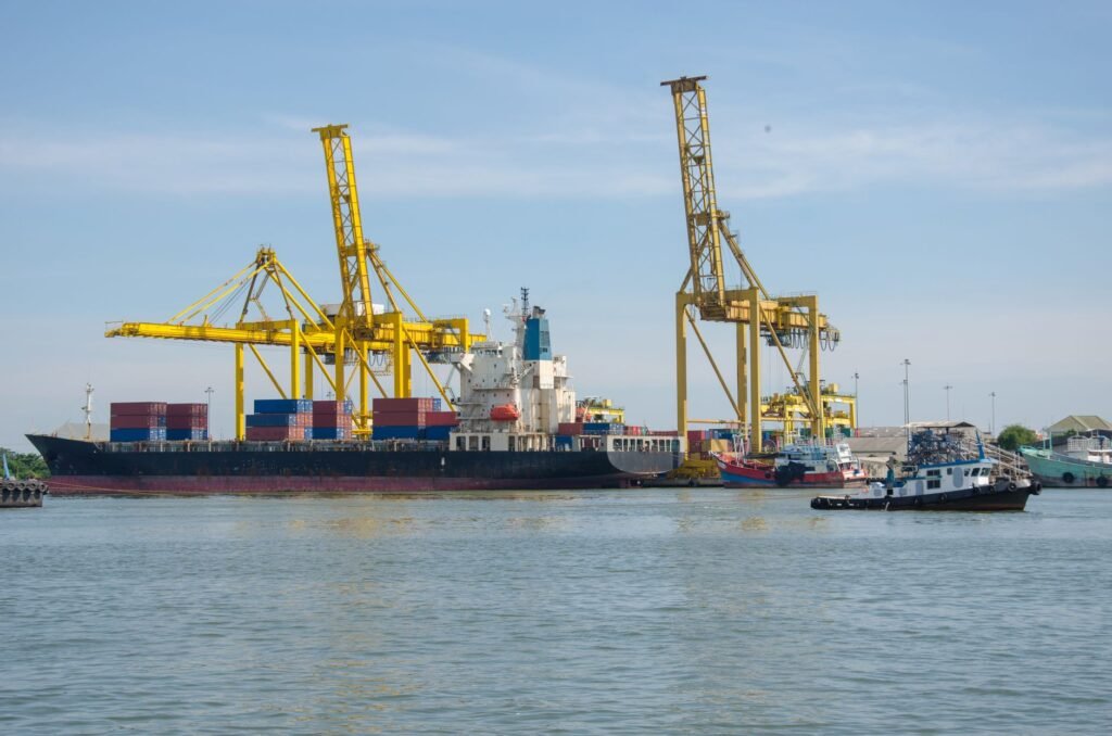 A cargo ship docked at an industrial port with cranes and containers, representing the Khalifa Port free zone